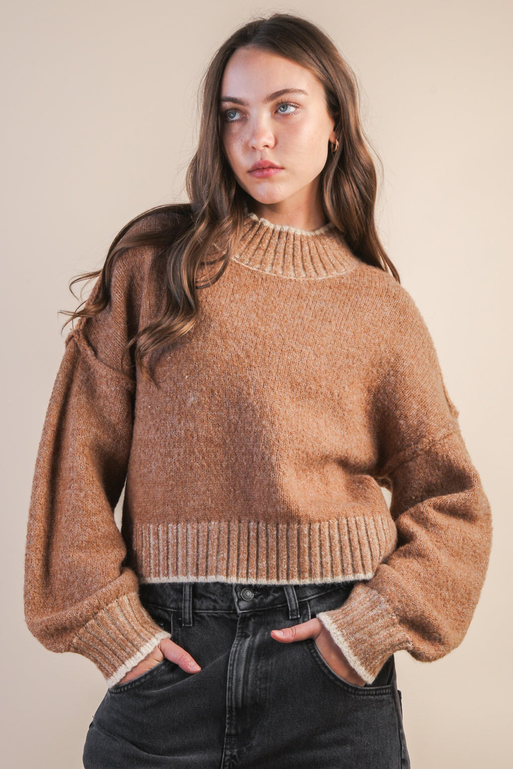 Woman wearing a mock neck mocha knit sweater with contrasting white trim against a plain background