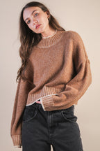 Woman wearing a mock neck mocha knit sweater with contrasting white trim against a plain background