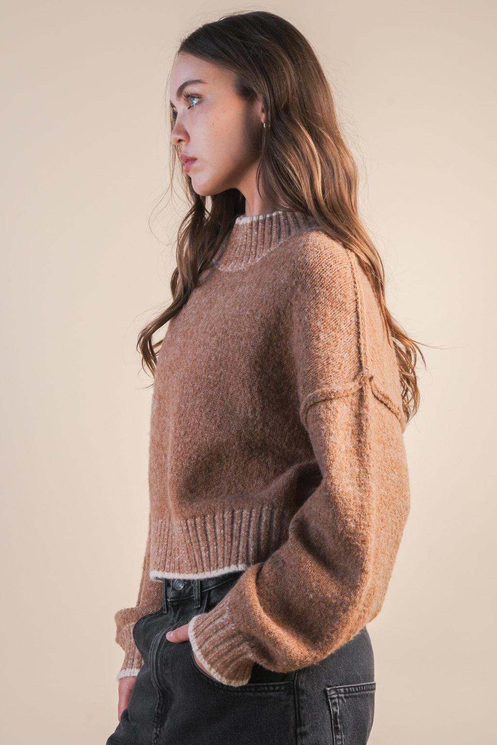 Woman wearing a mock neck mocha knit sweater with contrasting white trim against a plain background