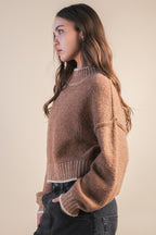 Woman wearing a mock neck mocha knit sweater with contrasting white trim against a plain background