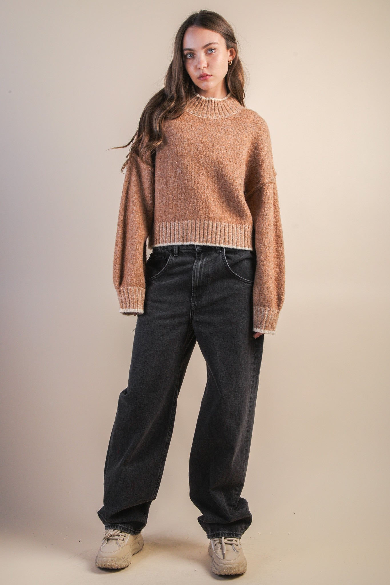 Woman wearing a mock neck mocha knit sweater with contrasting white trim and black jeans against a plain background