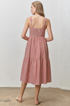 Back view of a woman wearing a red striped dress against a white wall.