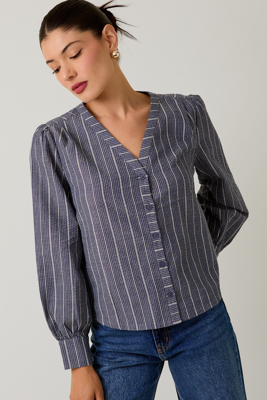 Woman wearing a navy striped blouse and jeans against a gray background