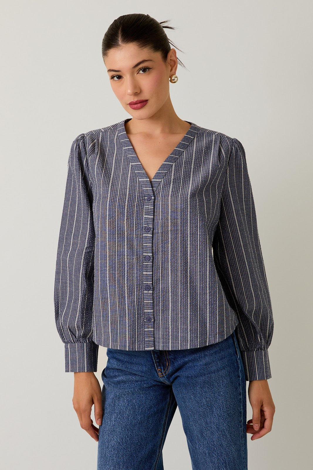 Woman wearing a navy striped blouse and jeans against a gray background