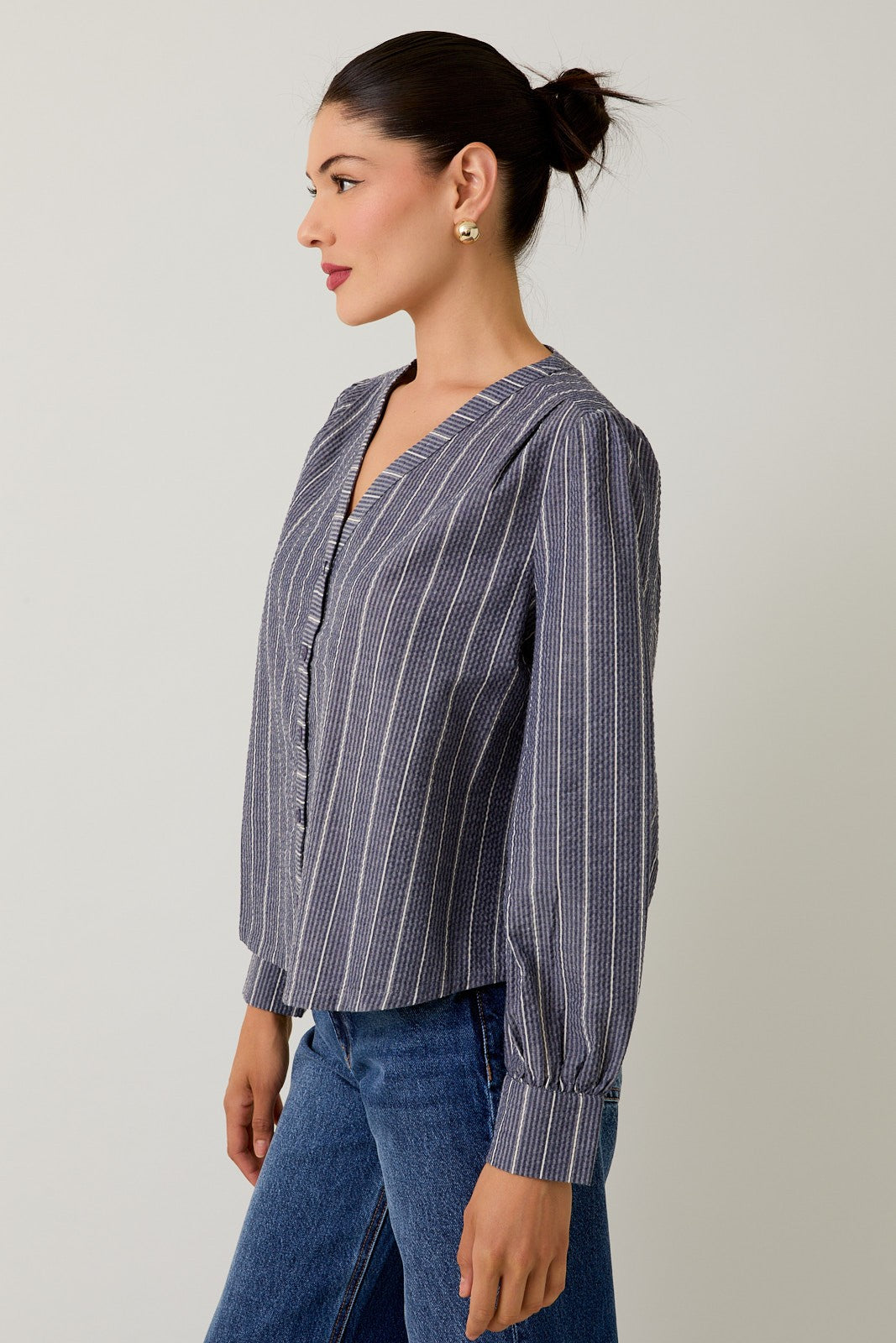Woman wearing a navy striped blouse and jeans against a gray background