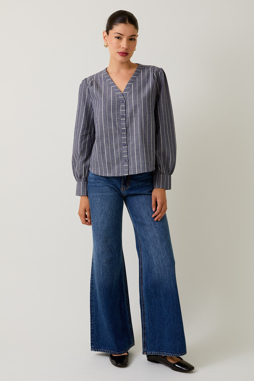 Woman wearing a navy striped blouse and jeans against a gray background