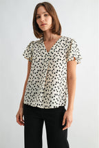 Woman wearing an ivory blouse with black floral pattern on a plain background