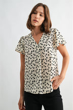 Woman wearing an ivory blouse with black floral pattern on a plain background