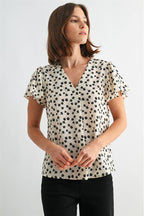 Woman wearing an ivory blouse with black floral pattern on a plain background
