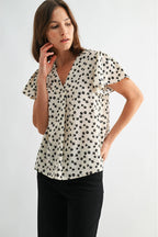 Woman wearing an ivory blouse with black floral pattern on a plain background