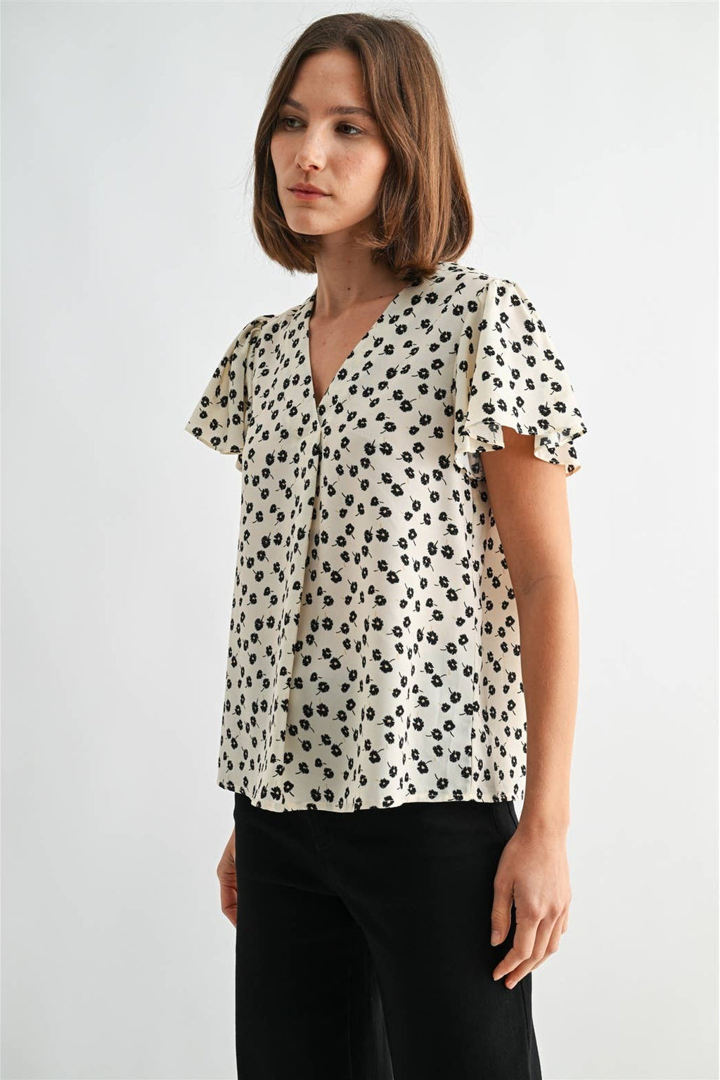 Woman wearing an ivory blouse with black floral pattern on a plain background
