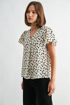 Woman wearing an ivory blouse with black floral pattern on a plain background