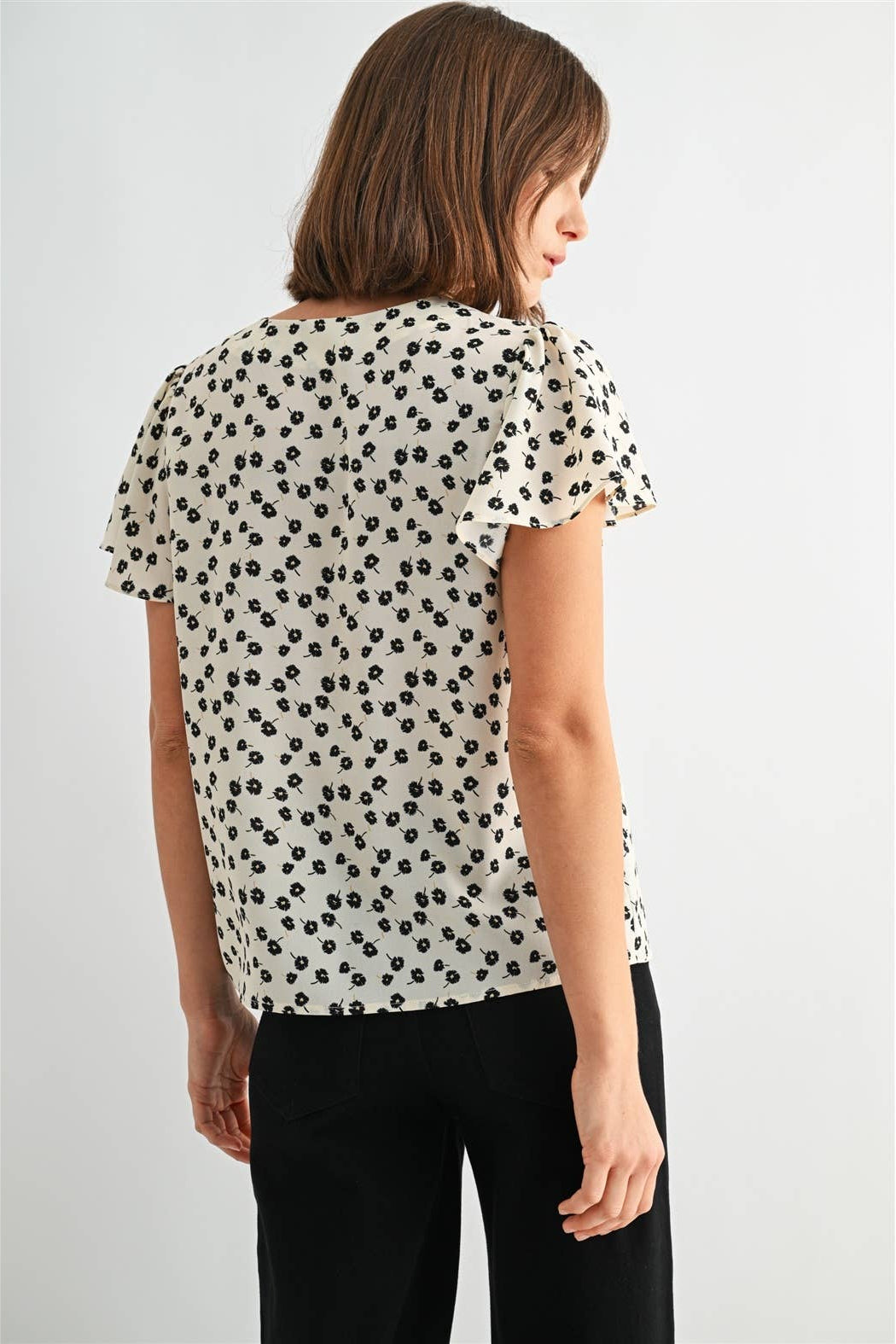 Back view of a woman wearing an ivory blouse with black floral pattern on a plain background