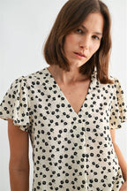 Woman wearing an ivory blouse with black floral pattern on a plain background
