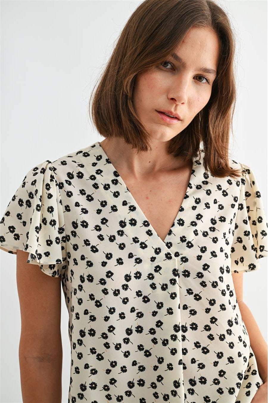 Woman wearing an ivory blouse with black floral pattern on a plain background