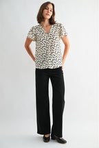 Woman wearing an ivory blouse with black floral pattern on a plain background