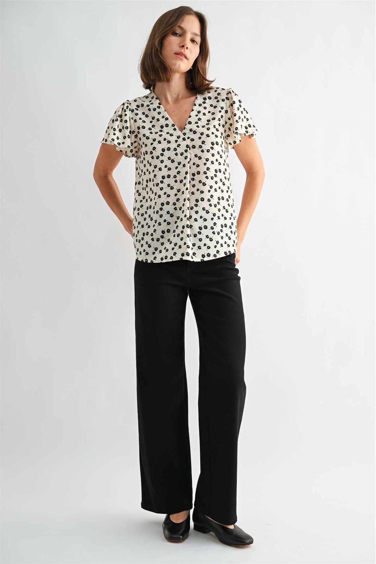 Woman wearing an ivory blouse with black floral pattern on a plain background