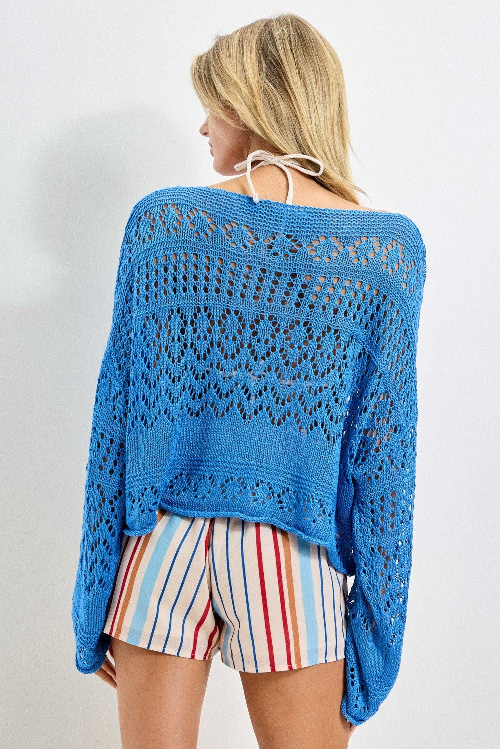 Back view of  a woman wearing an azure  blue crochet top and striped shorts on a white background