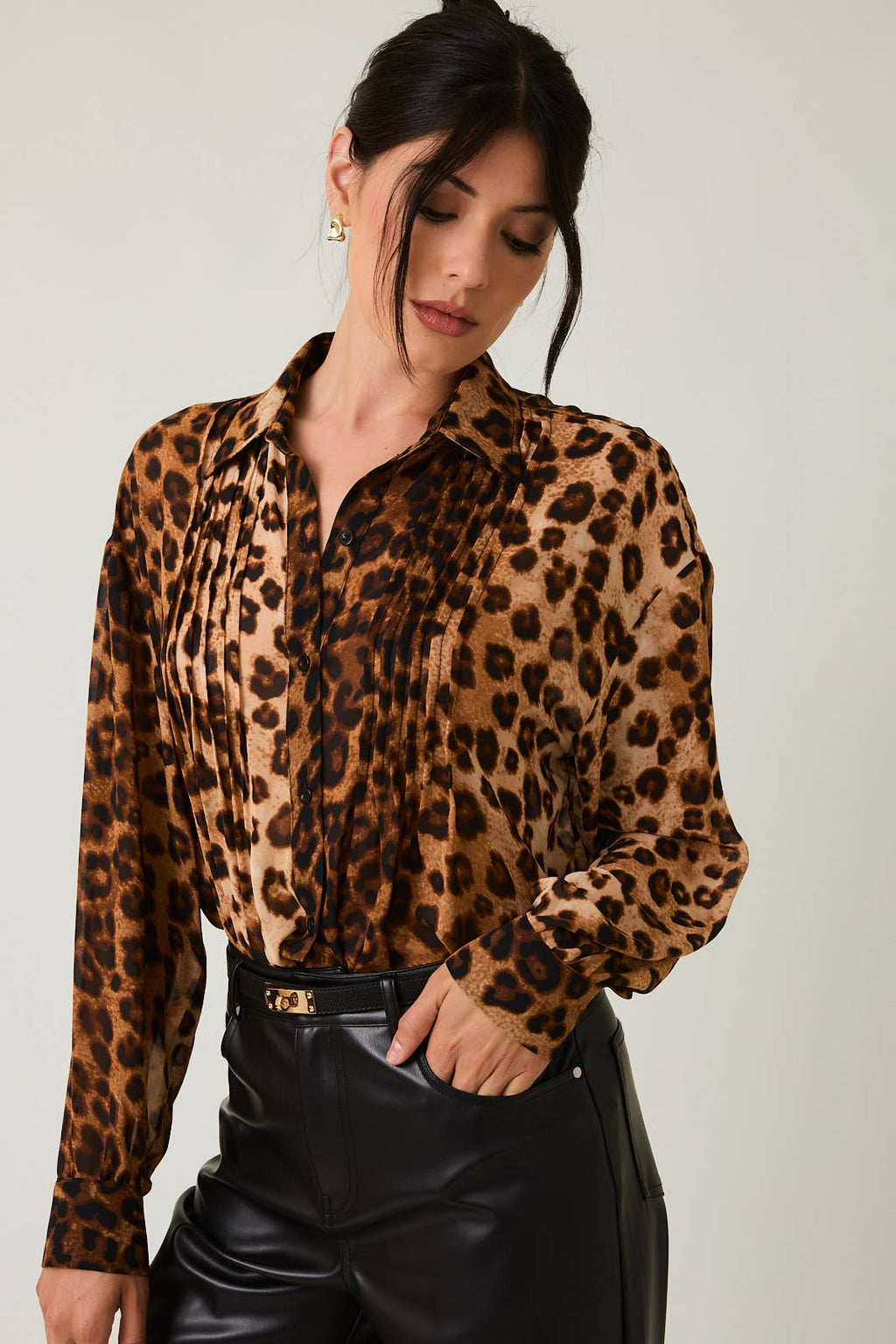 Woman wearing a leopard print blouse and black leather pants against a plain background