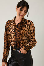 Woman wearing a leopard print blouse and black leather pants against a plain background