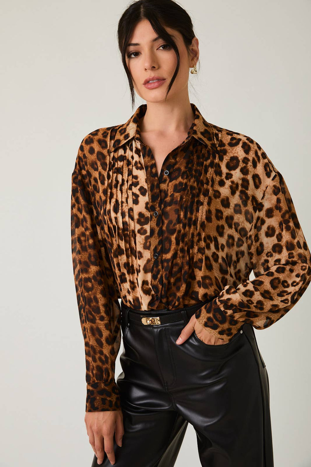 Woman wearing a leopard print blouse and black leather pants against a plain background