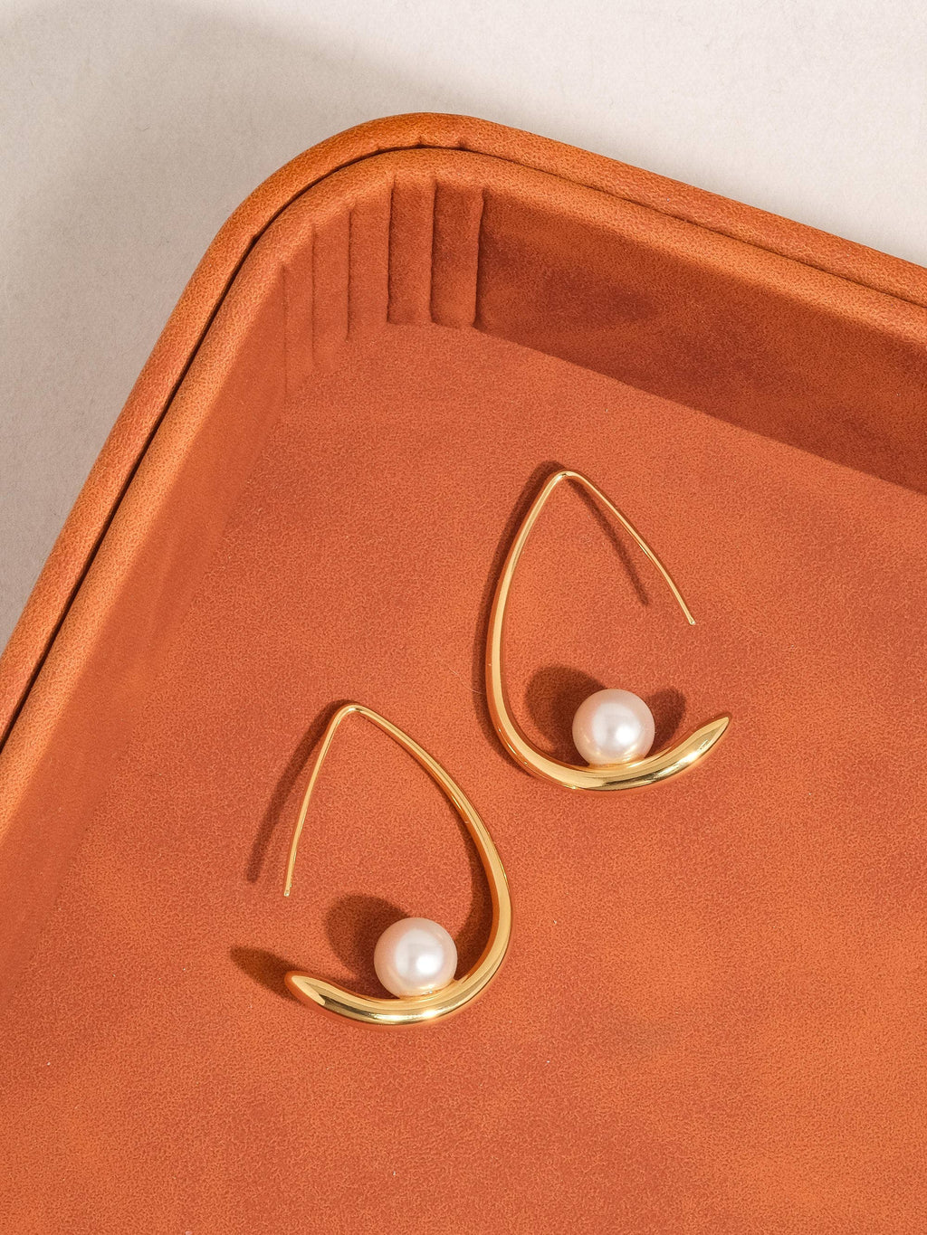 Gold earrings with pearls suspended on gold-plated hoop on an orange background