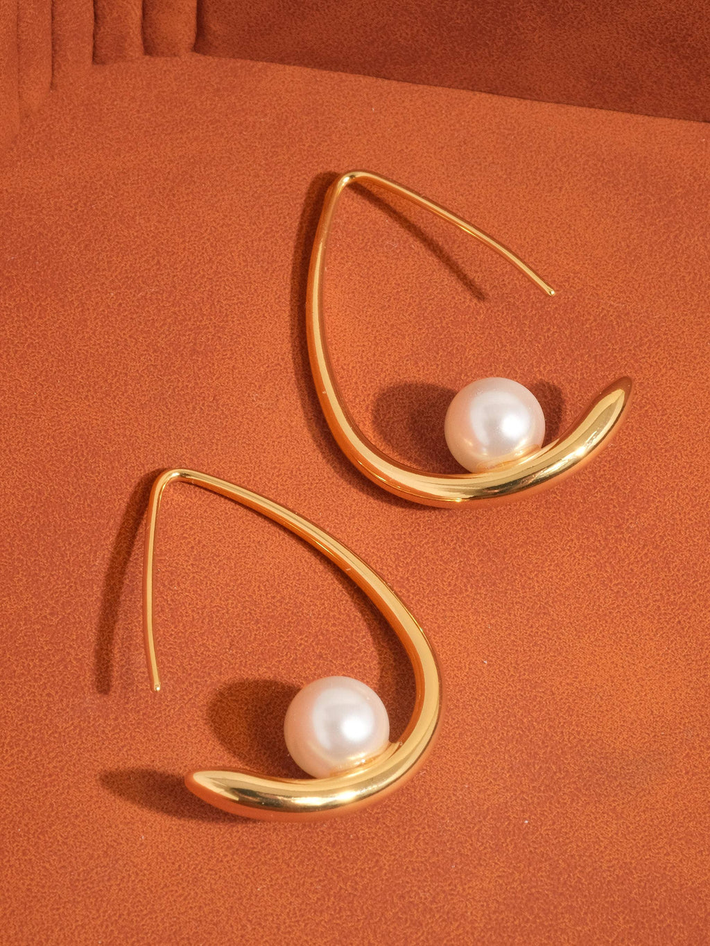 Gold earrings with pearls suspended on gold-plated hoop on an orange background