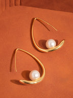 Gold earrings with pearls suspended on gold-plated hoop on an orange background