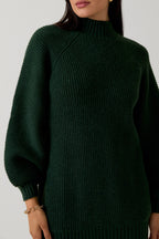 Woman wearing a hunter green sweater dress against a plain background