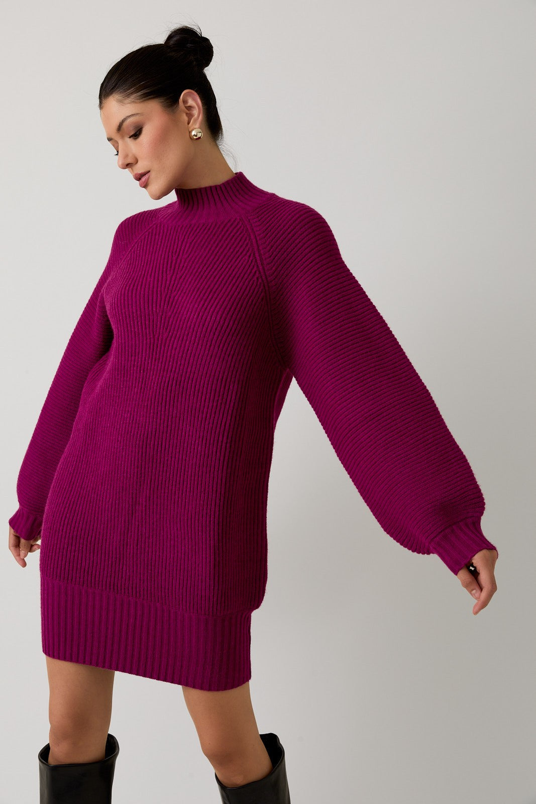 Woman wearing a magenta mock neck raglan balloon sleeve sweater dress against a plain background