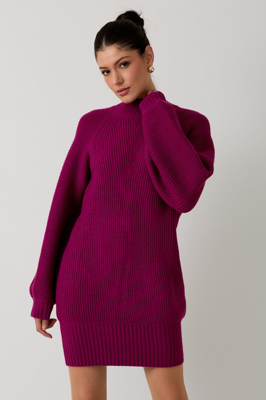 Woman wearing a magenta mock neck raglan balloon sleeve sweater dress against a plain background