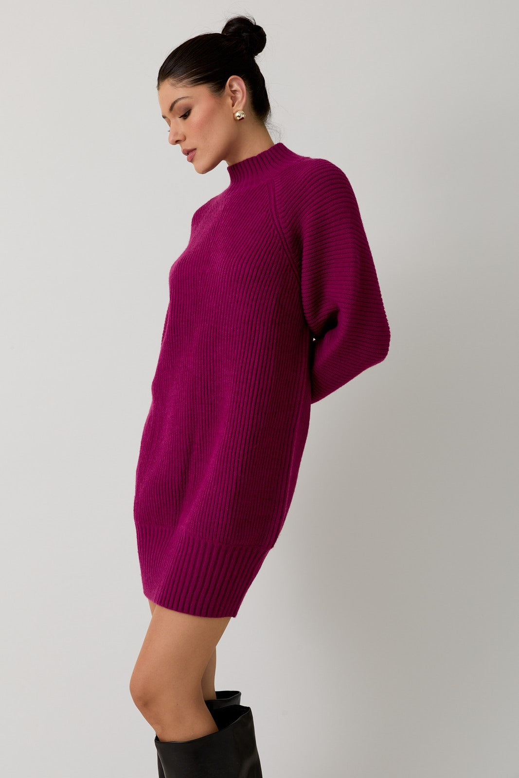 Woman wearing a magenta mock neck raglan balloon sleeve sweater dress against a plain background