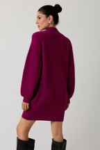 Back view of a woman wearing a magenta mock neck raglan balloon sleeve sweater dress against a plain background