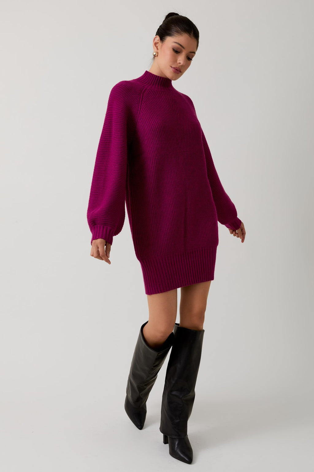 Woman wearing a magenta mock neck raglan balloon sleeve sweater dress and black boots against a plain background