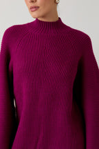 Woman wearing a magenta mock neck raglan balloon sleeve sweater dress against a plain background