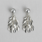 Pair of silver tone  leaf-shaped tassel earrings with ball stud on a light gray background