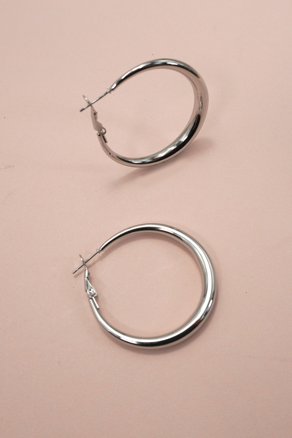 Silver puffy hoop earrings on a pink background