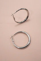 Silver puffy hoop earrings on a pink background