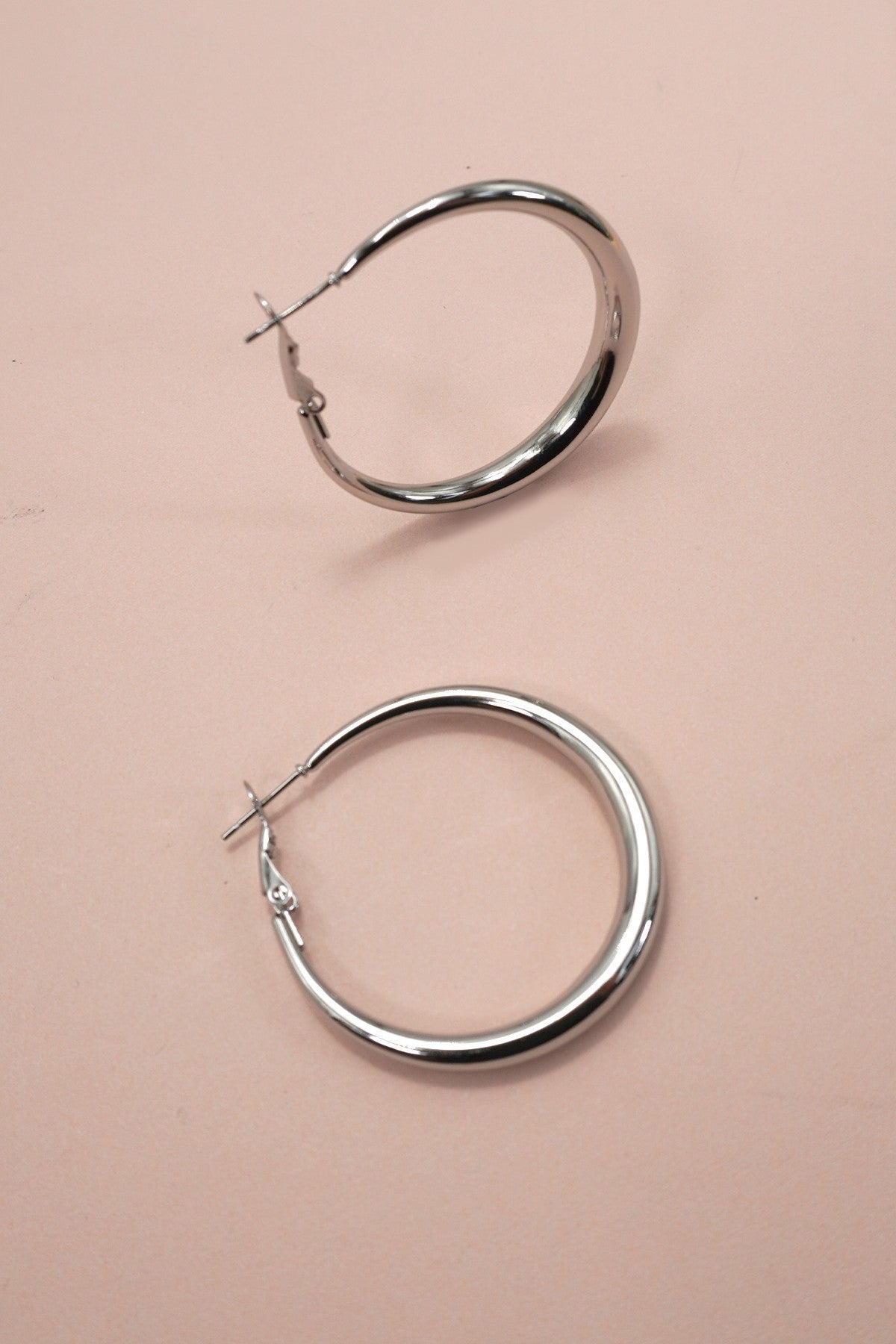 Silver puffy hoop earrings on a pink background