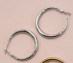 Silver puffy hoop earrings on a pink background