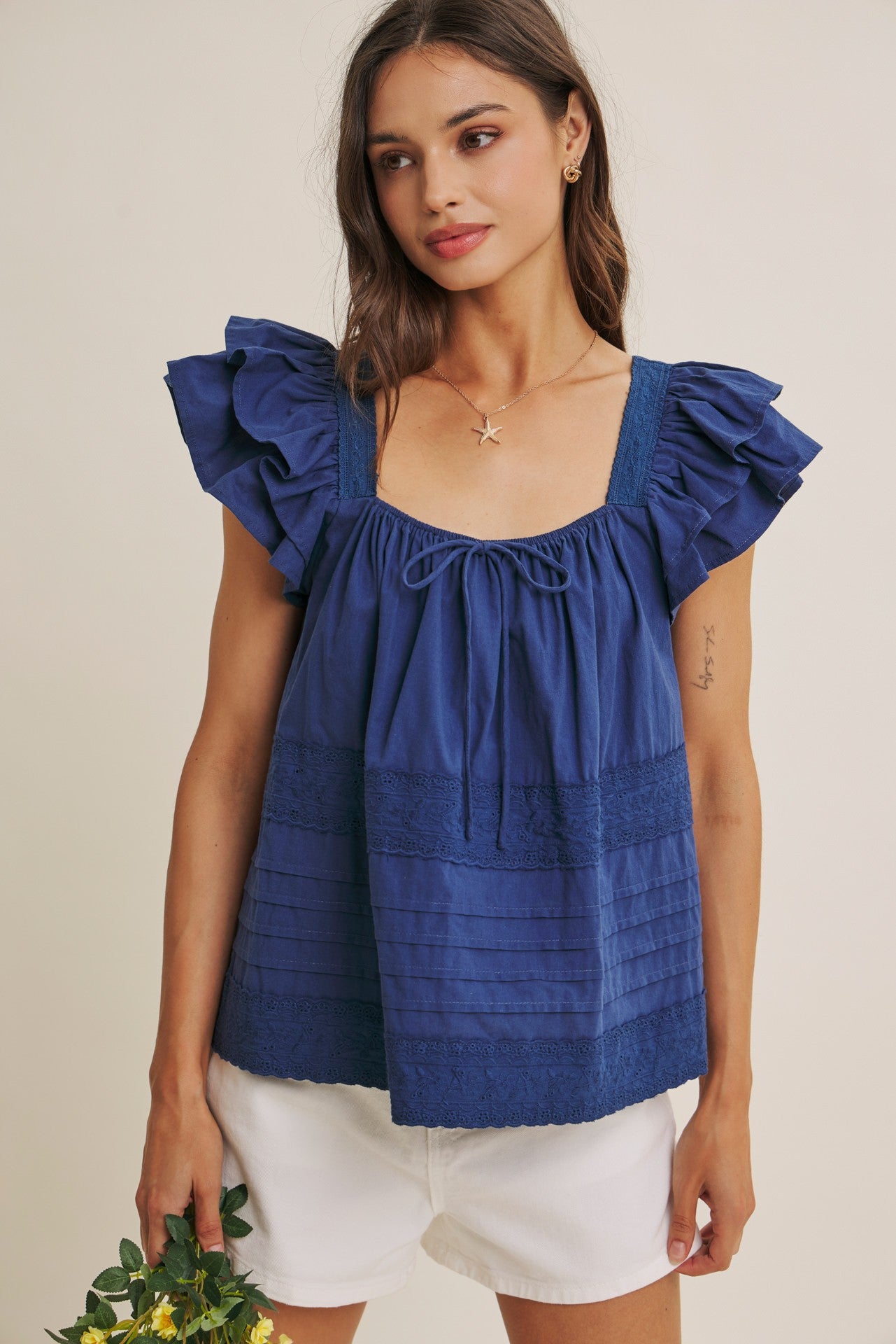 Woman wearing a midnight blue top with ruffled sleeves against a beige background