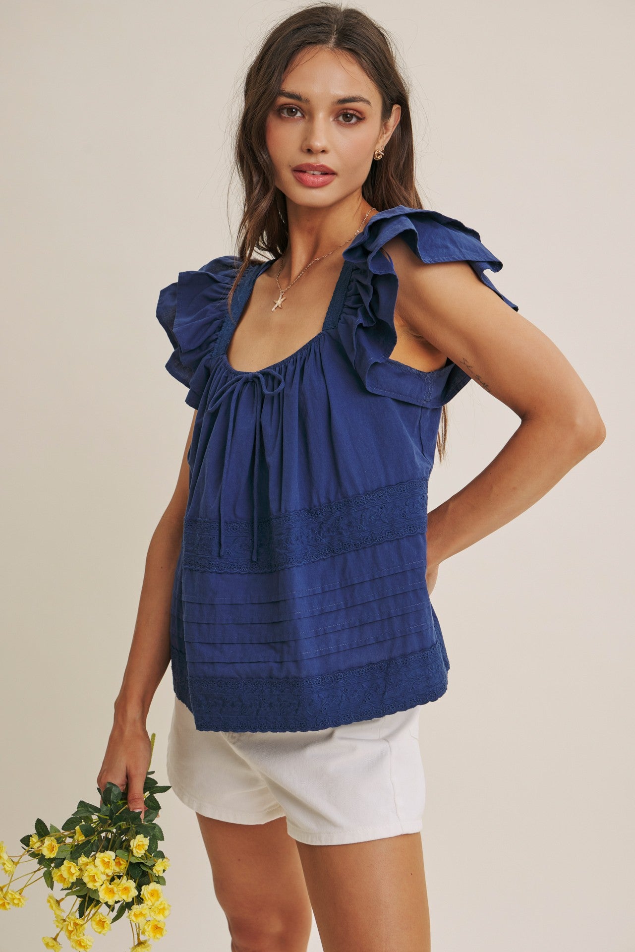 Woman wearing a midnight blue top with ruffled sleeves against a beige background