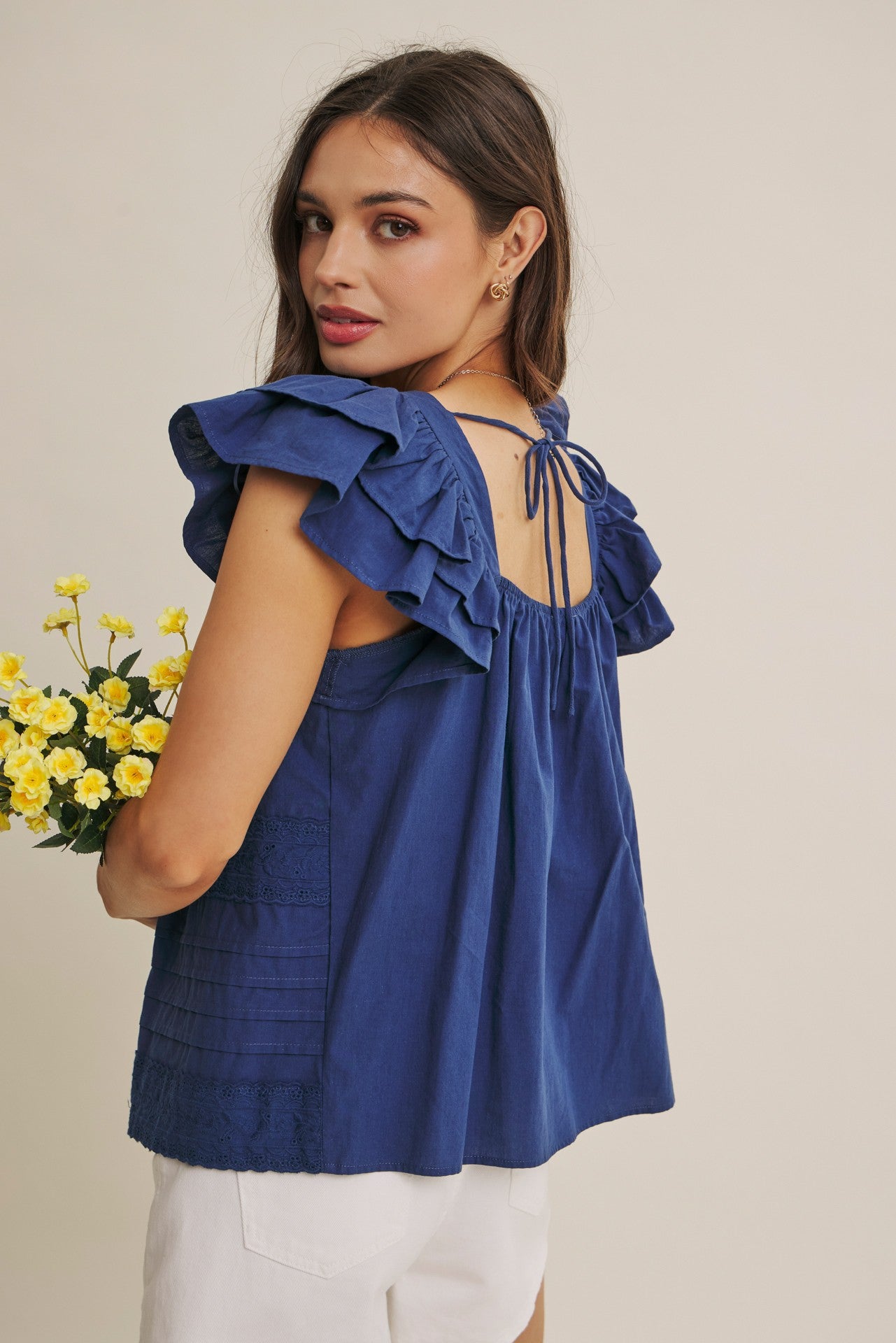 Woman wearing a blue top with ruffled sleeves and open back, holding yellow flowers.