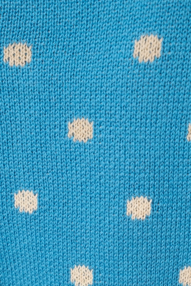 A close-up of a blue knit fabric with a repeating pattern of small cream-colored polka dots.