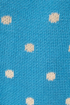 A close-up of a blue knit fabric with a repeating pattern of small cream-colored polka dots.