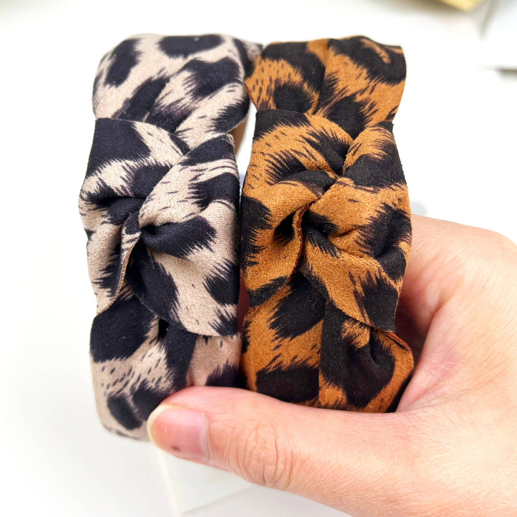 Women's two leopard print top knot headbands held by a hand against a white background