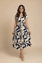 A woman wearing a  midi dress with a navy blue leaf pattern on an off-white background, standing in front of a storefront.