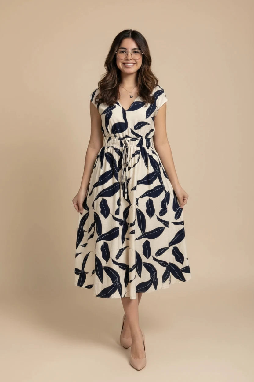 A woman wearing a  midi dress with a navy blue leaf pattern on an off-white background, standing in front of a storefront.