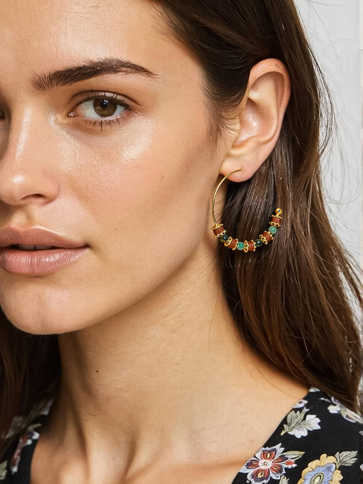 A close-up of a woman wearing a large gold hoop earring adorned with small colorful gemstones, including green, orange, and red.