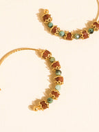 Gold hoop earrings with alternating textured brown and green faceted beads, displayed on a warm cream background.